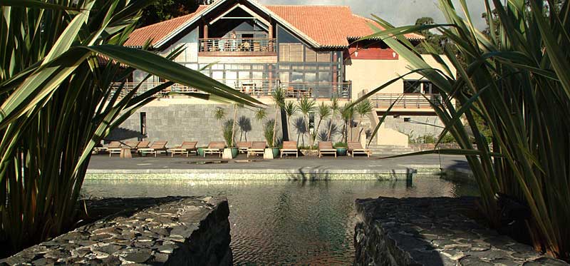 Durch subtropische Pflanzen fotografierter Pool mit Hauptgebäude des Choupana Hills